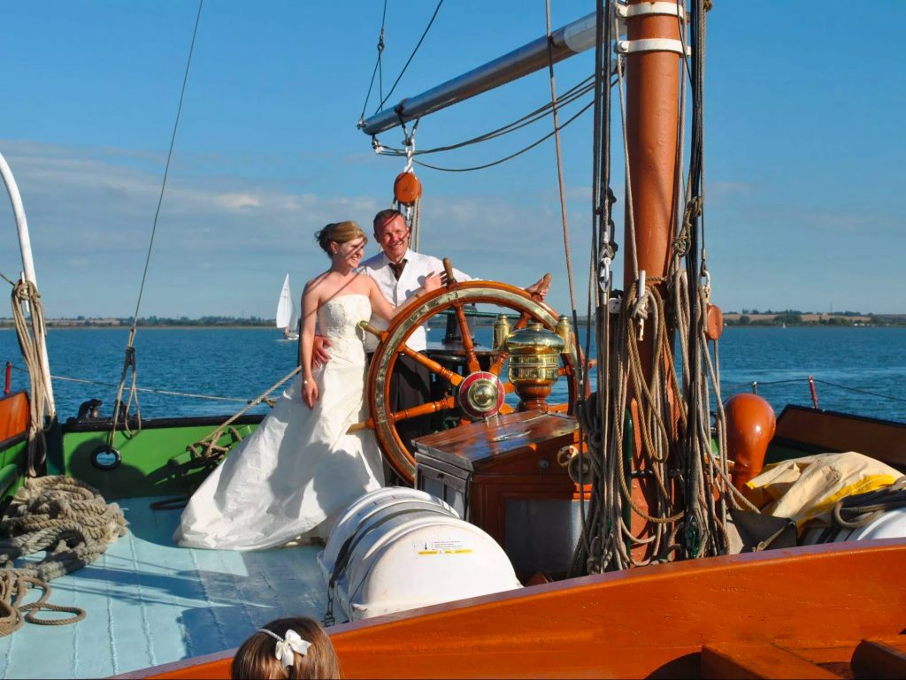 Wedding reception onboard a vintage sailing barge on the river with guests and scenic salt marsh views